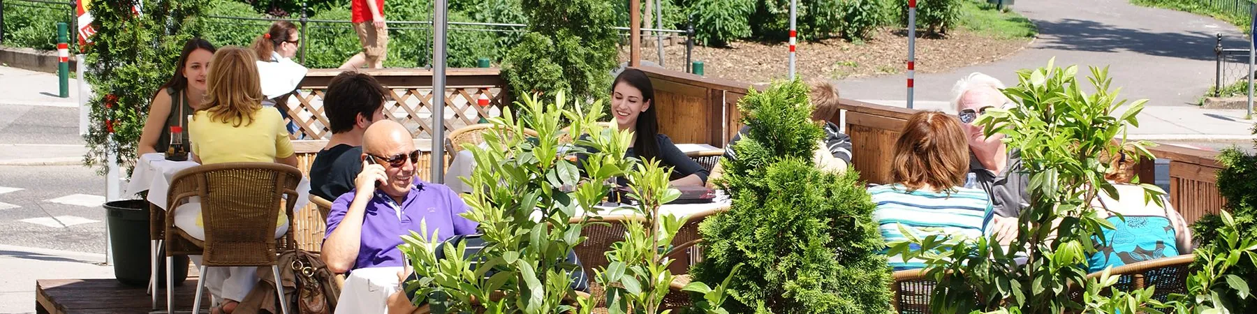Gäste im begrünten Gastgarten an einem Sommertag