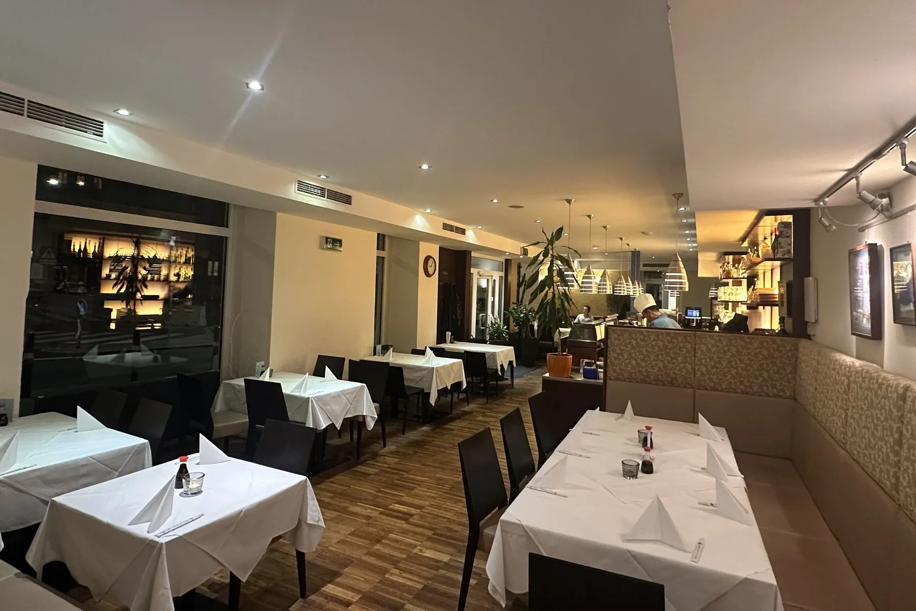 Gastraum am Abend mit eingedeckten Tischen und dem Koch an der offenen Sushi-Bar